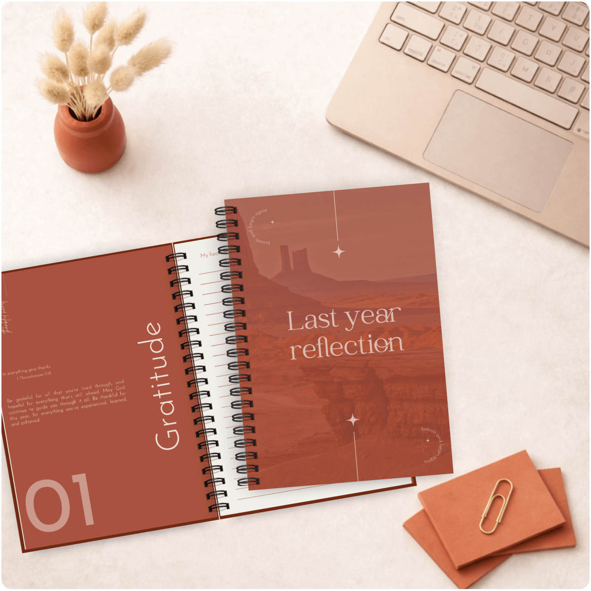 Open spiral-bound notebook titled 'Last year reflection' on a desk with a laptop and decorative items.
