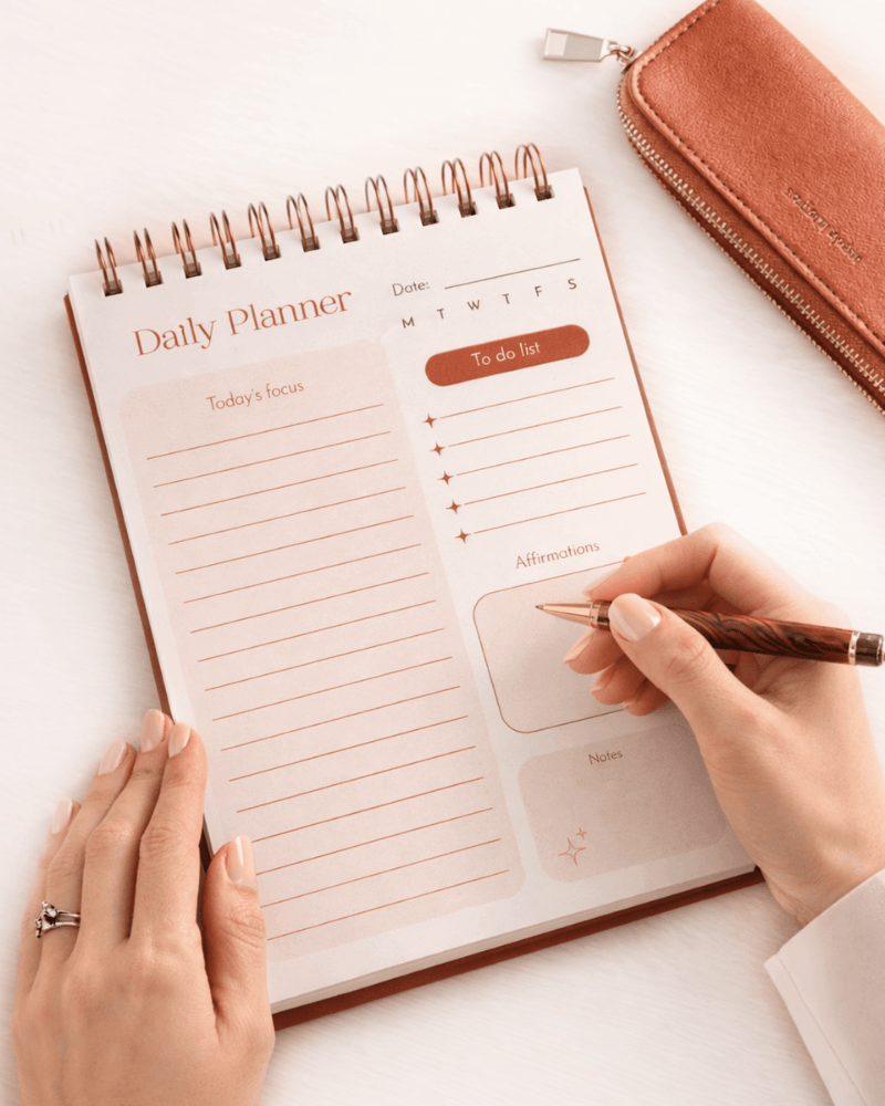 Daily planner with a hand holding a pen on a white surface