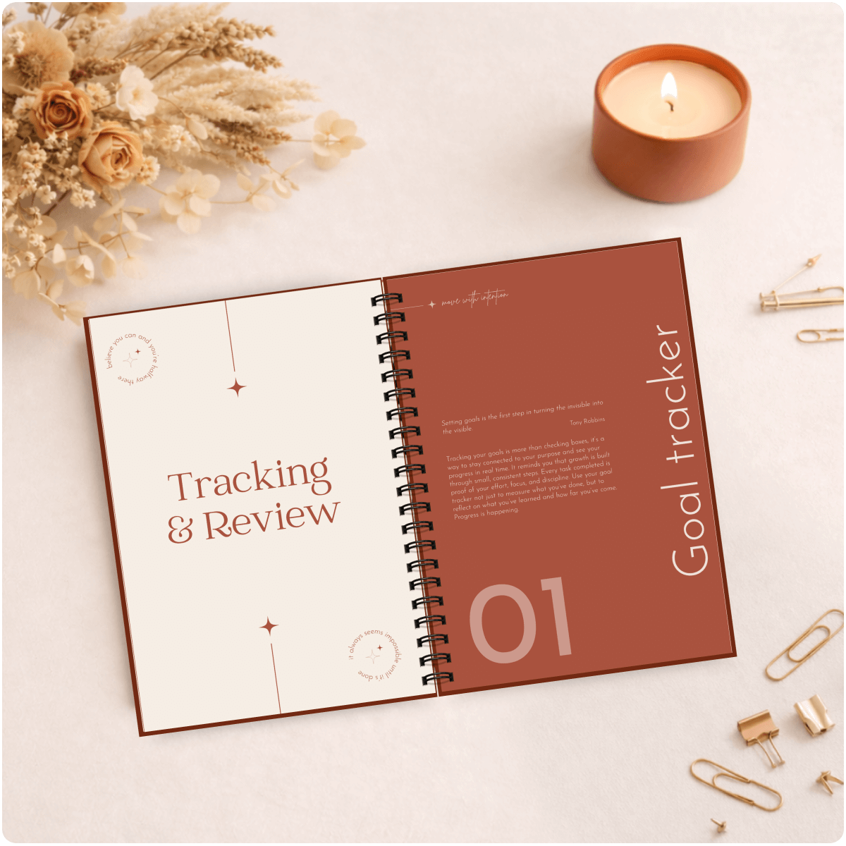 Open spiral-bound notebook with 'Tracking & Review' and 'Goal tracker' sections on a light surface with decorative items.